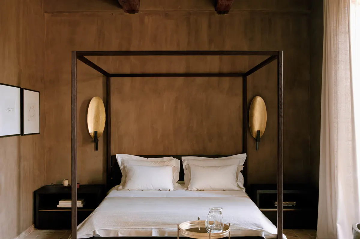 Canopy bed with dark wood frame and brass wall sconces in warm earth-toned room