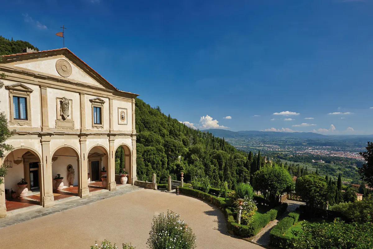 Cream building with arched loggia, stone ornaments, and panoramic view of the Florence valley beyond cypress