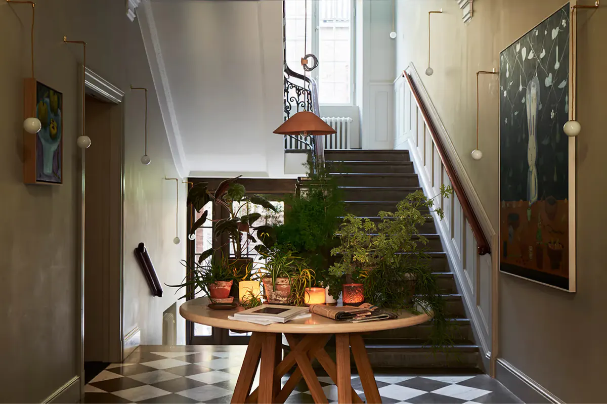 A cream hallway with potted plants on a round wooden table beneath a staircase