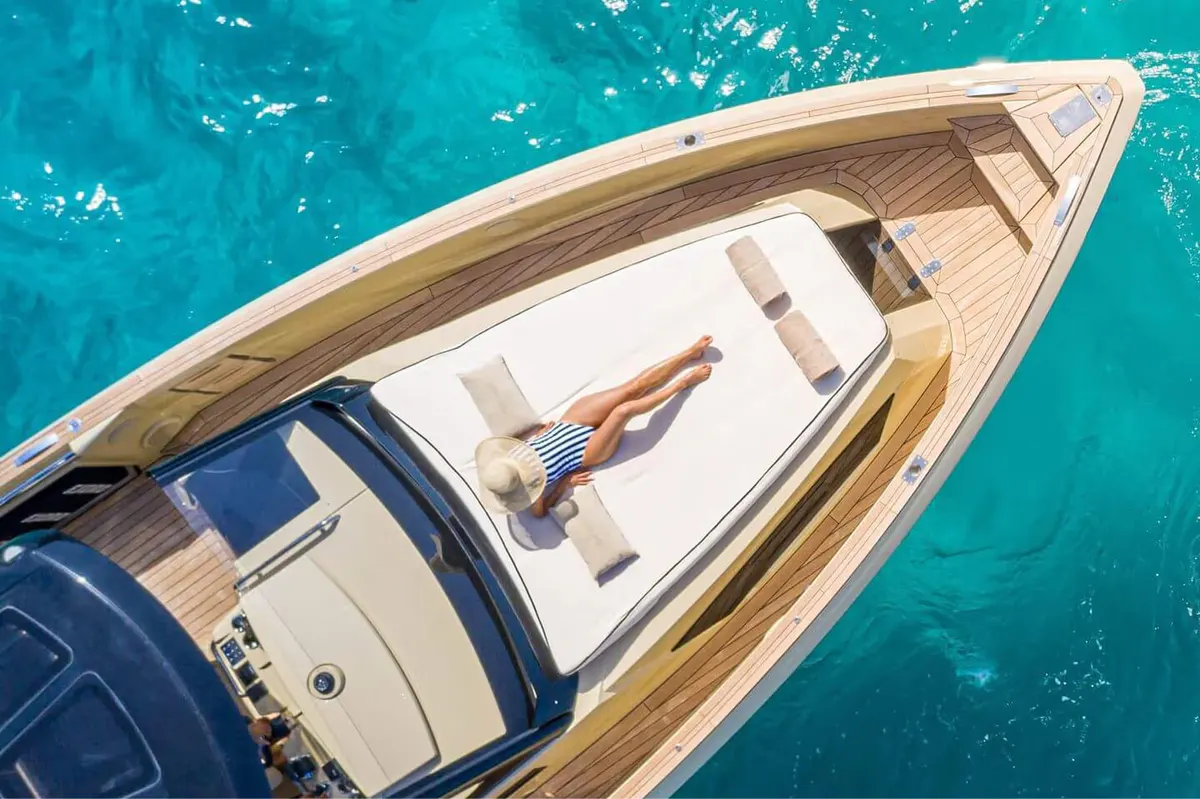 A gleaming white yacht hull overhead shows glass windows and the transparent turquoise sea