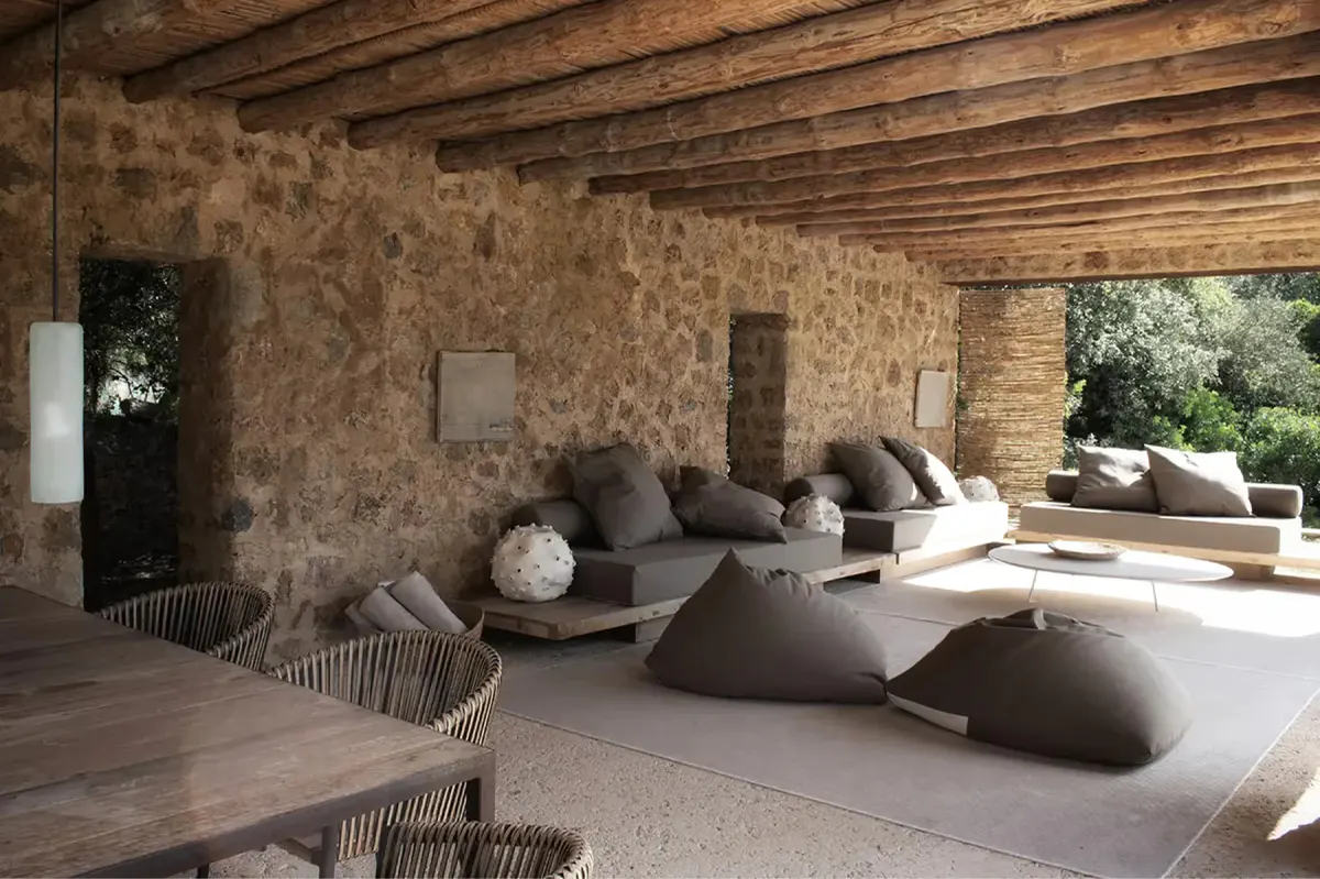 Covered outdoor lounge with curved concrete seating, timber framework, and natural stone walls