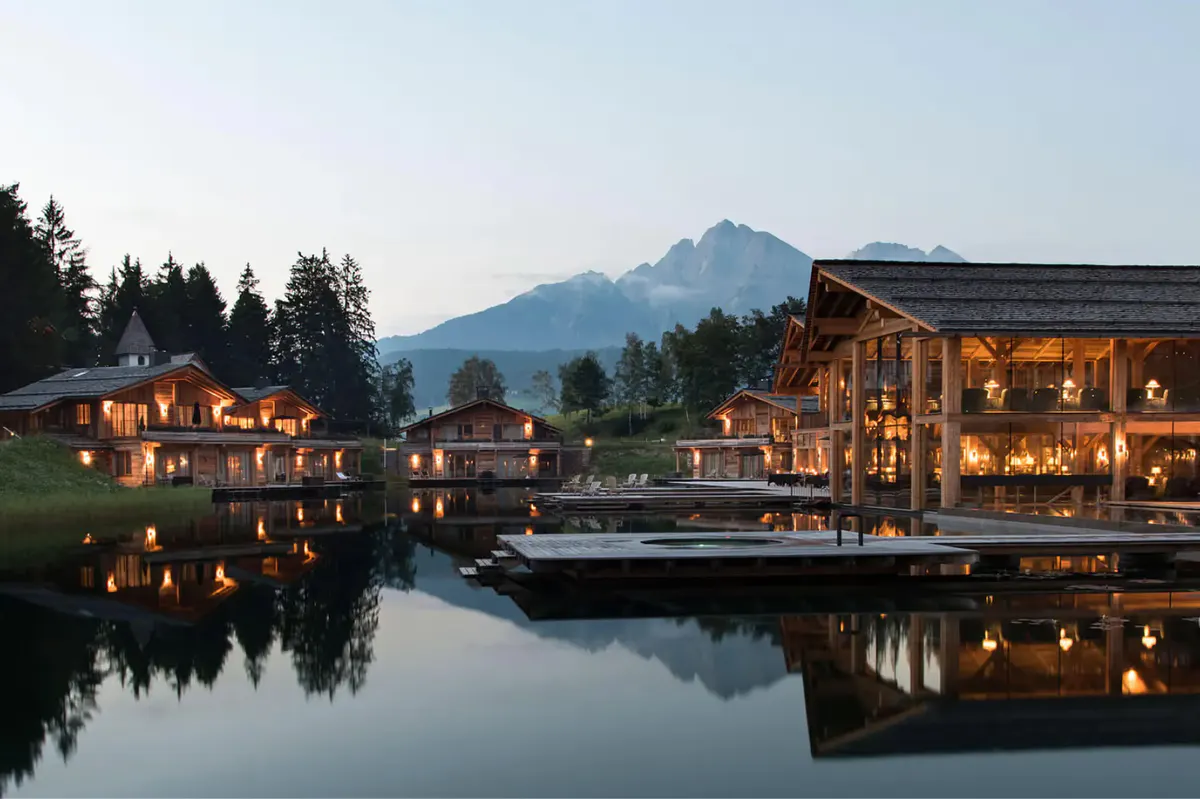 The hotel lit at dusk beside a reflective lake with mountains behind