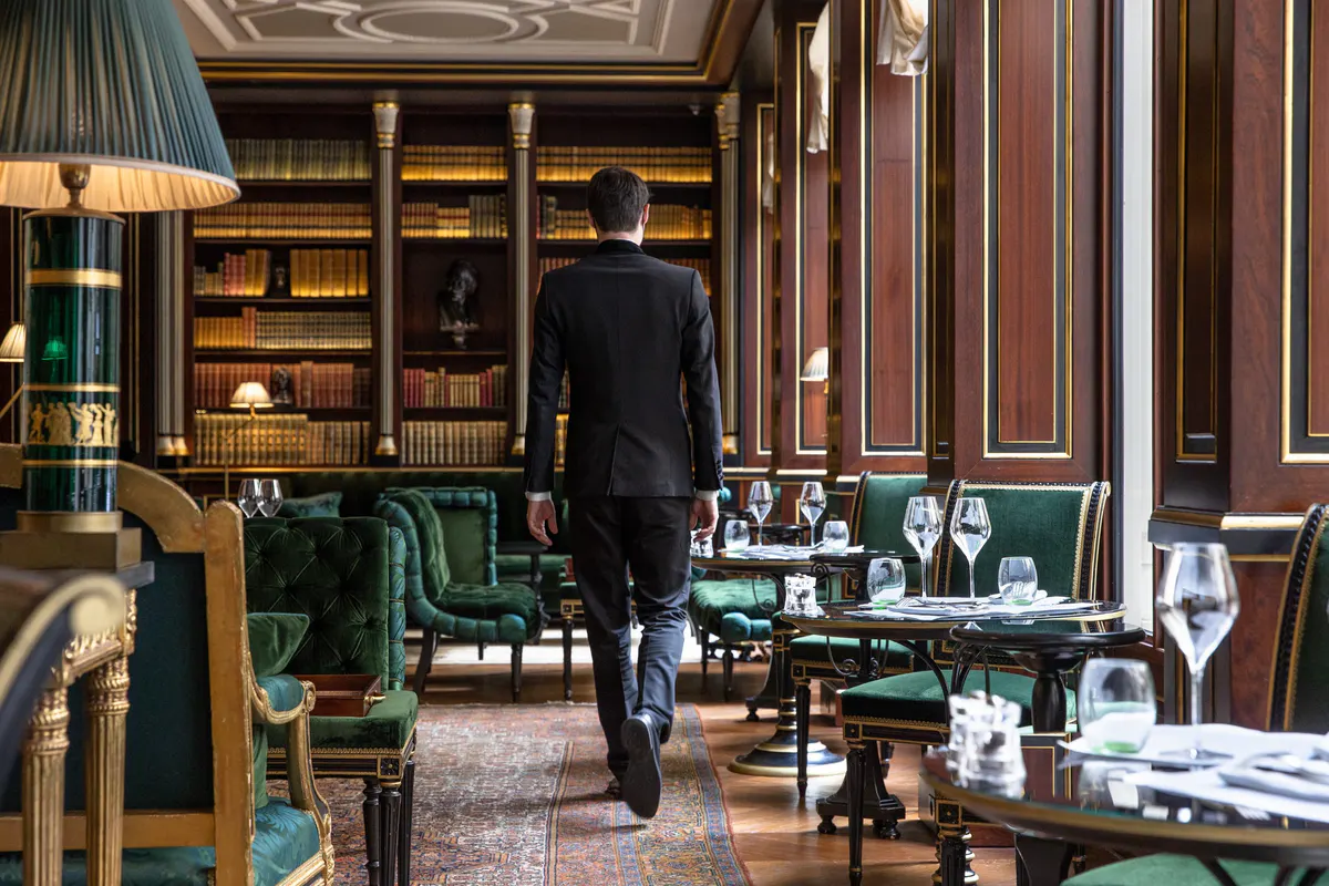The dining room with dark wood walls, green furniture, and gilded library shelving