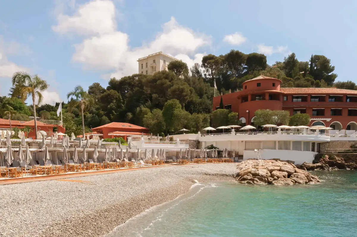 Beach access with sand and turquoise water, rocky cliffs and hotel structures