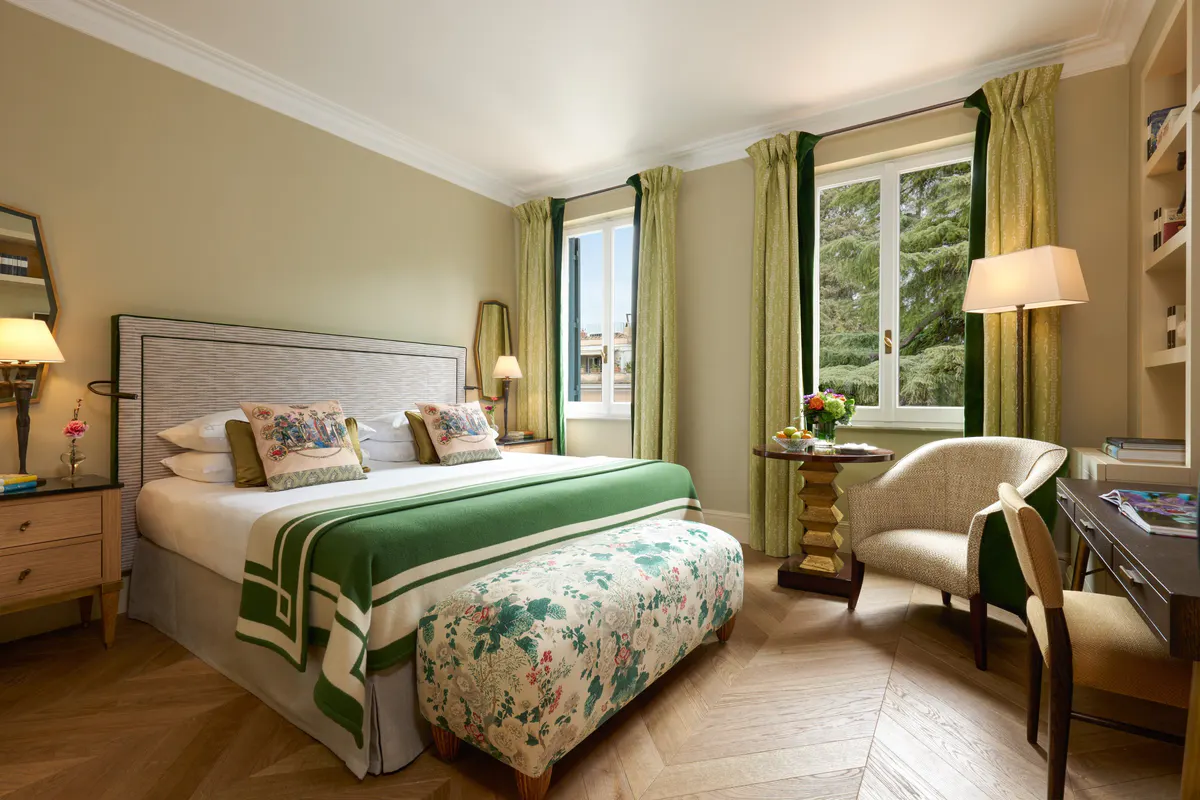 Bedroom with green headboard, patterned fabrics, and seating by window with garden view