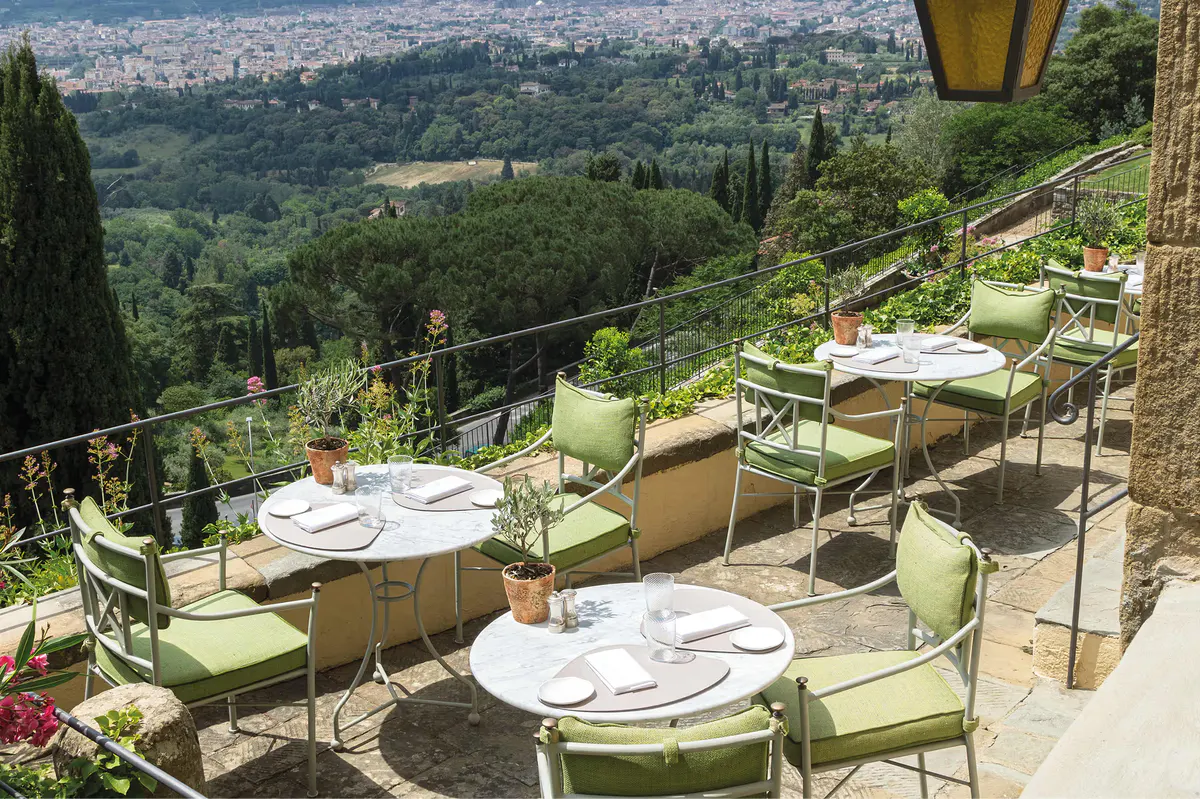 Outdoor dining terraces with green chairs, white tablecloths, and sweeping views over the Tuscan landscape