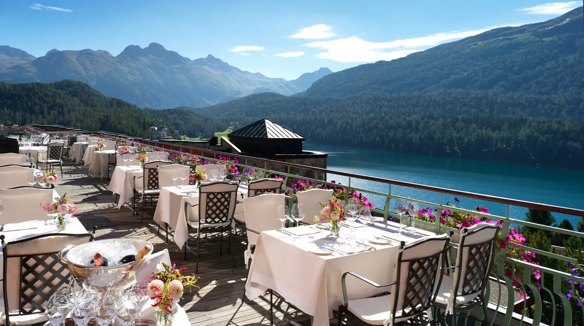 Outdoor terrace with white tablecloths overlooking blue lake and snow-capped peaks